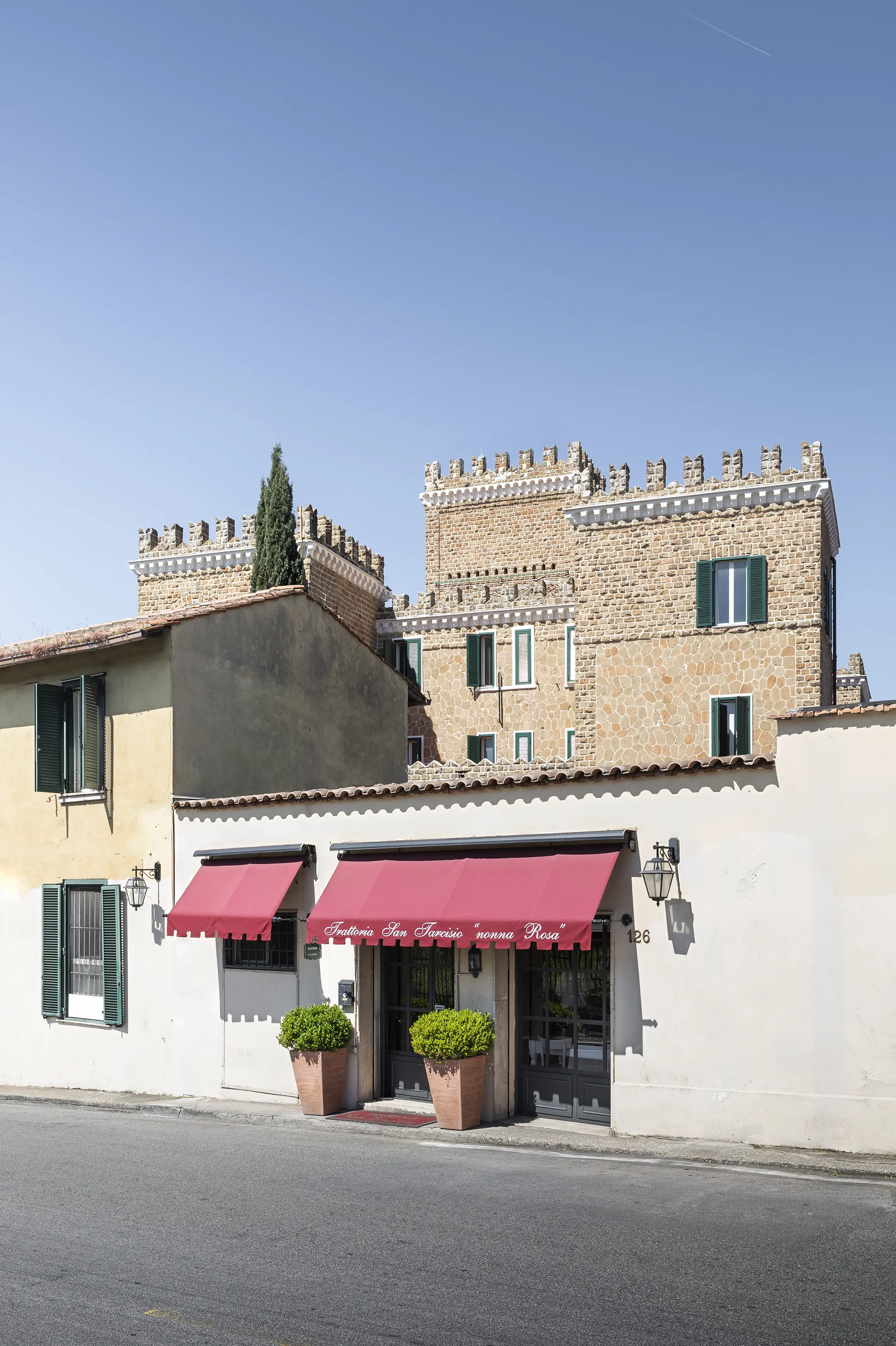Facade of a building with red awnings reading Trattoria San Tarcisio nonna Rosa under clear blue sky.