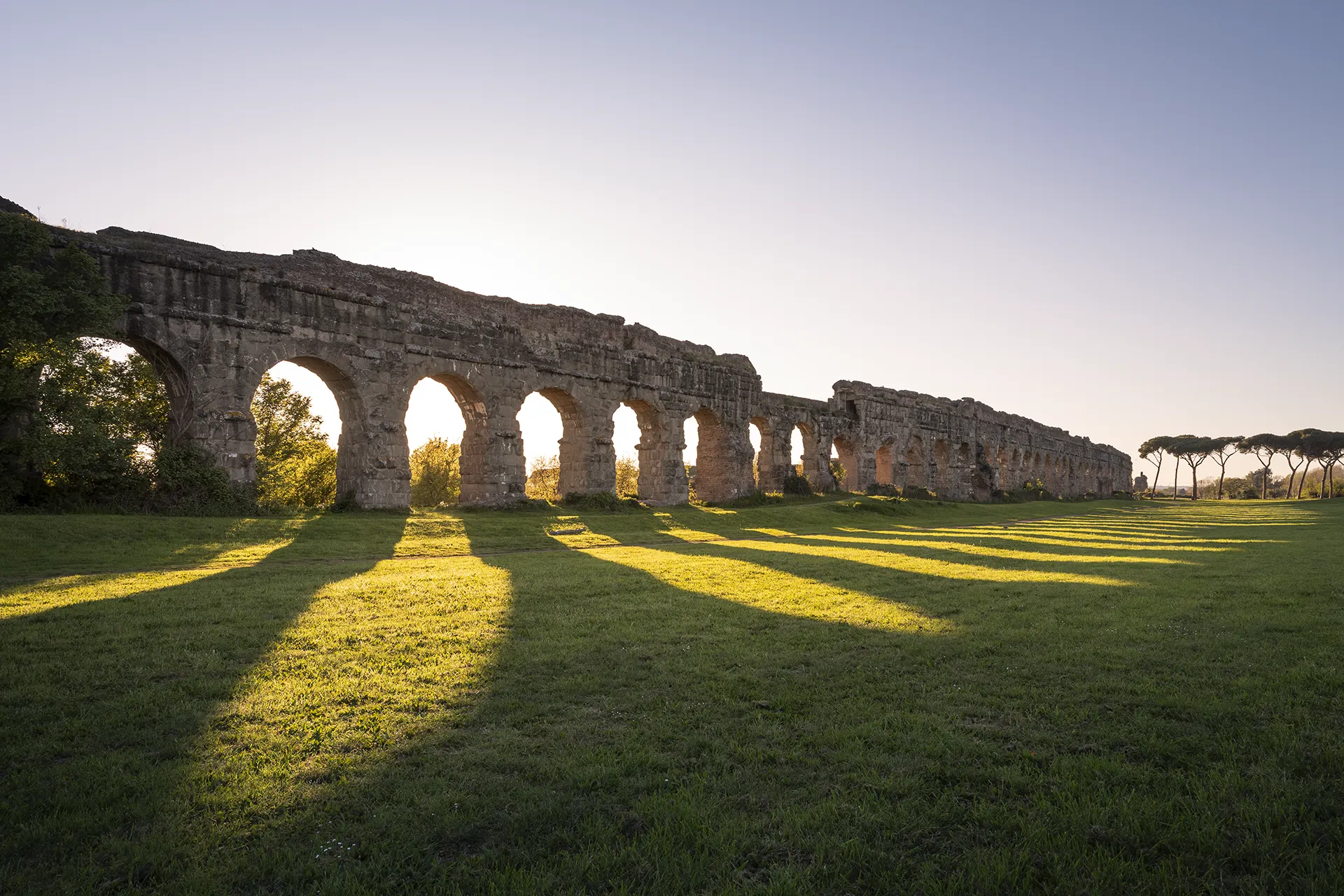 Ancient stone aqueduct casting long shadows on grass in the late afternoon sunlight.
