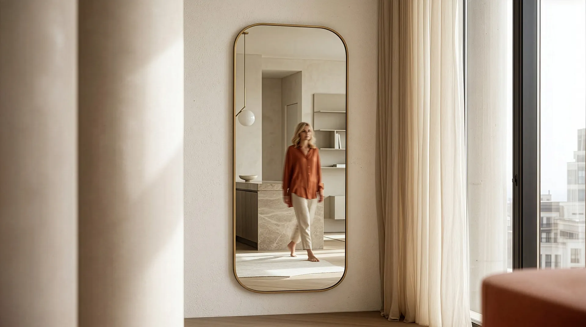 Full-length mirror on wall reflecting a woman walking barefoot in a softly lit modern room.