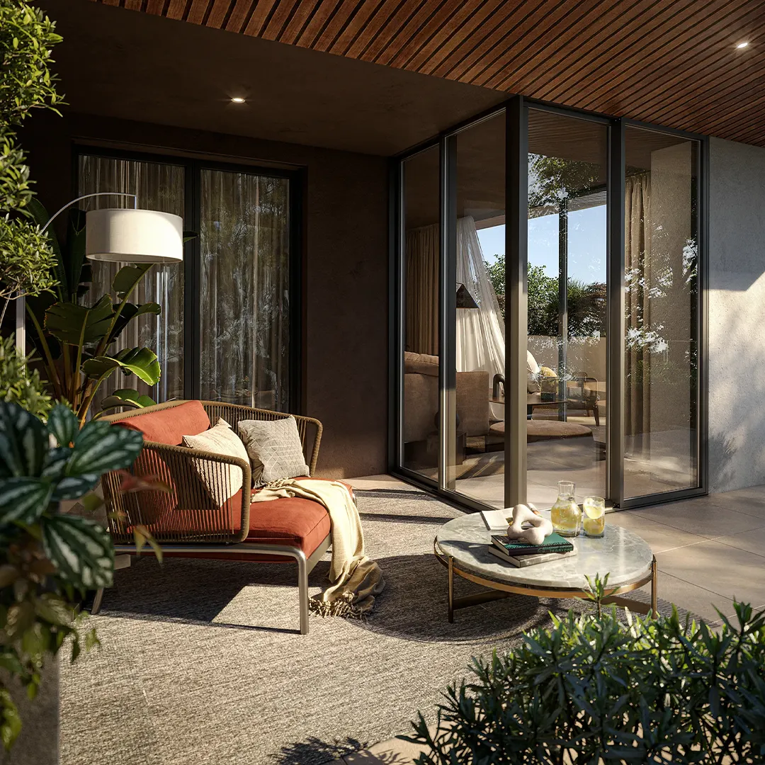 Outdoor patio with a rust-colored cushioned chair, pillows, table with books, and glass doors opening indoors.